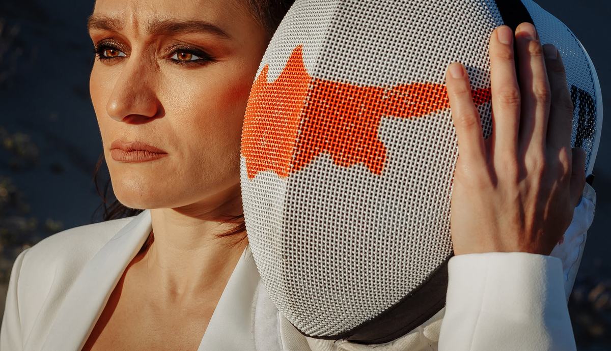 Adult fencer holding a Cyprus-flag mask beside her face