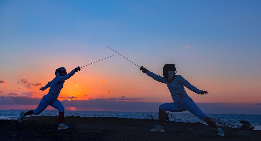 Two fencers lunging at each other at dusk by the sea