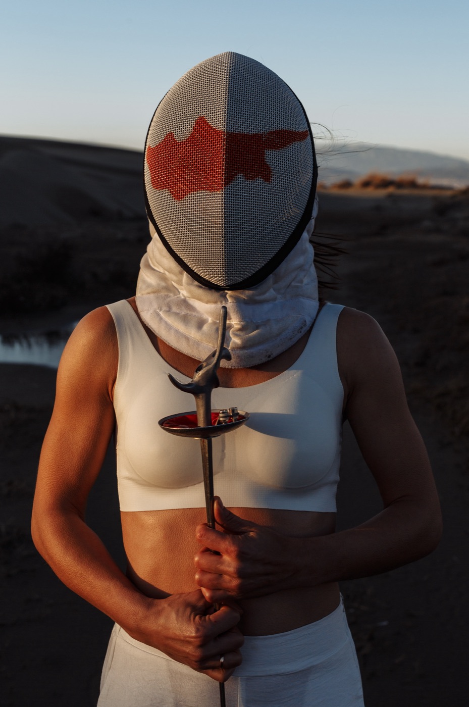 Fencer in a Cyprus-flag mask holding a foil at sunset